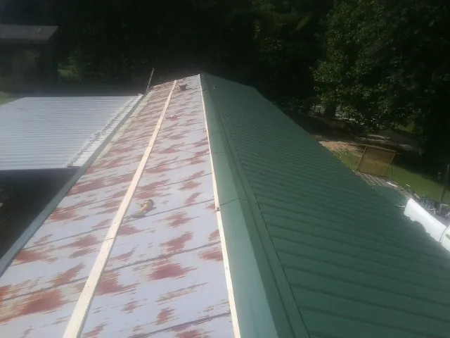Old rusted panels beside newly installed green metal roofing — Wind Damage Roof Repair by Roofing Brothers in Hardyville