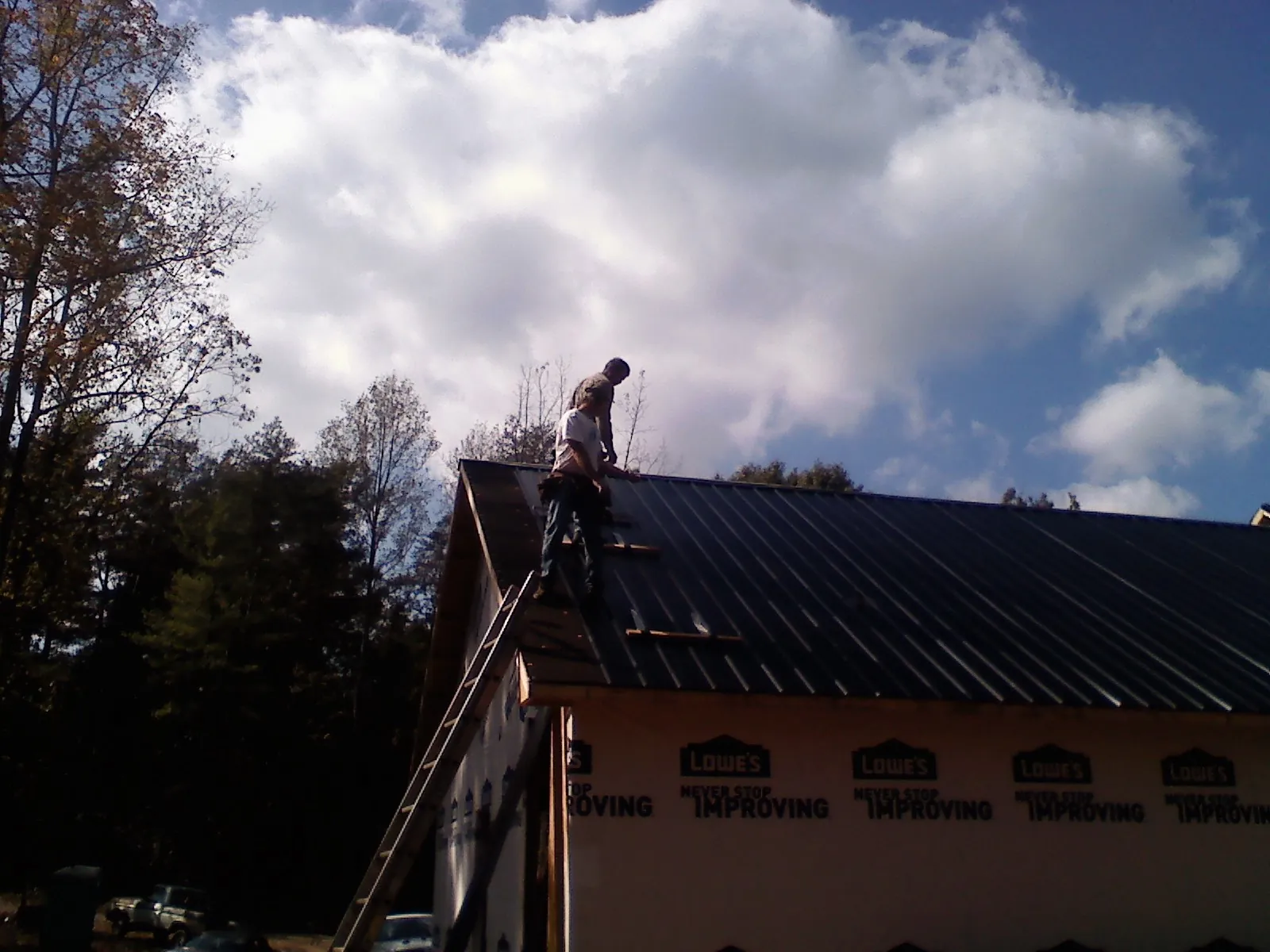 Roofer fastening dark metal panels high against a cloudy sky, from a Roof Inspection job in Hardyville